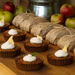 Small desserts with white cream and lemon slices on a wooden surface with wrapped packages and apples in the background.